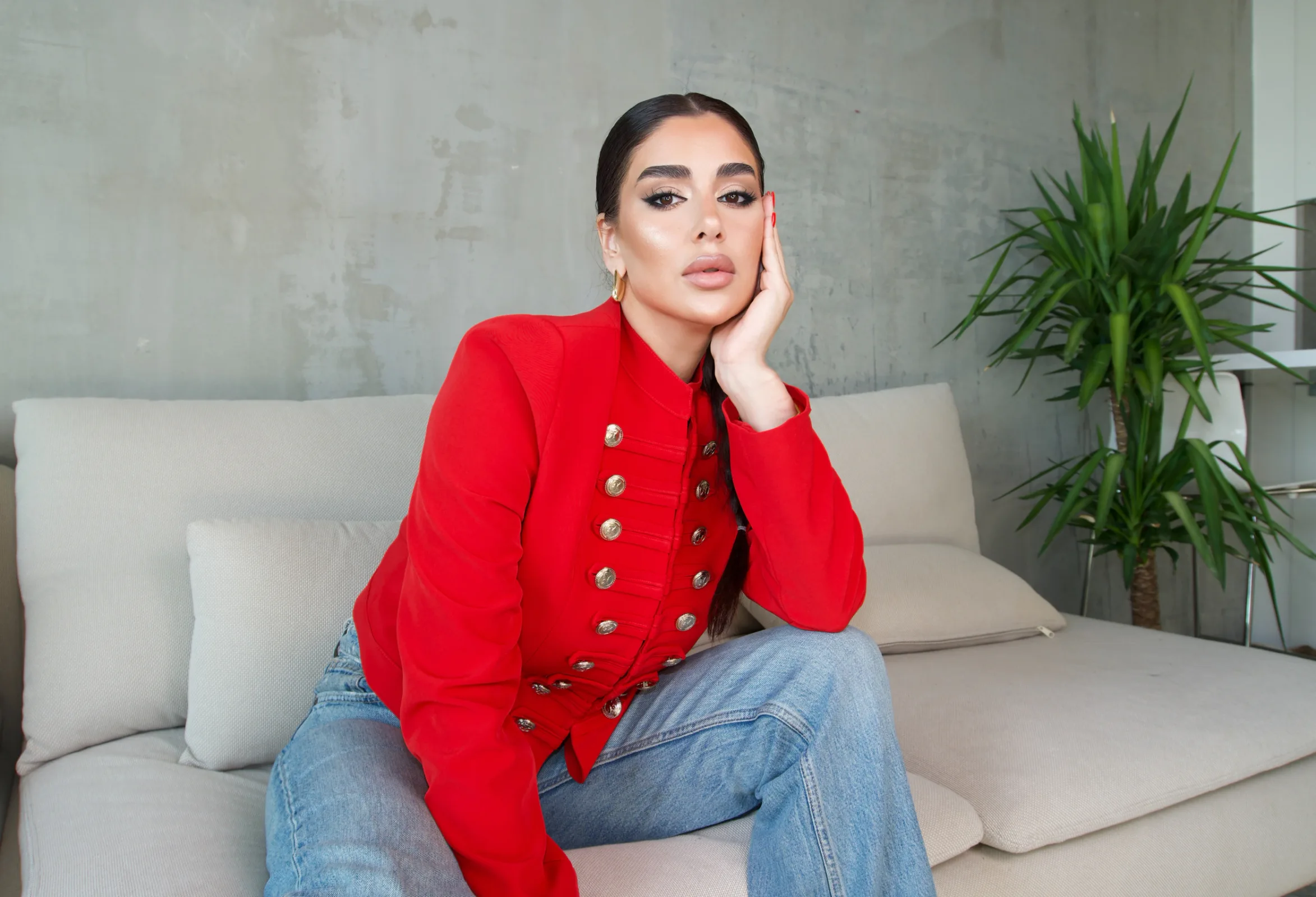 Red bandsman jacket with twin rows of gold buttons, worn with light denim on a cream sofa