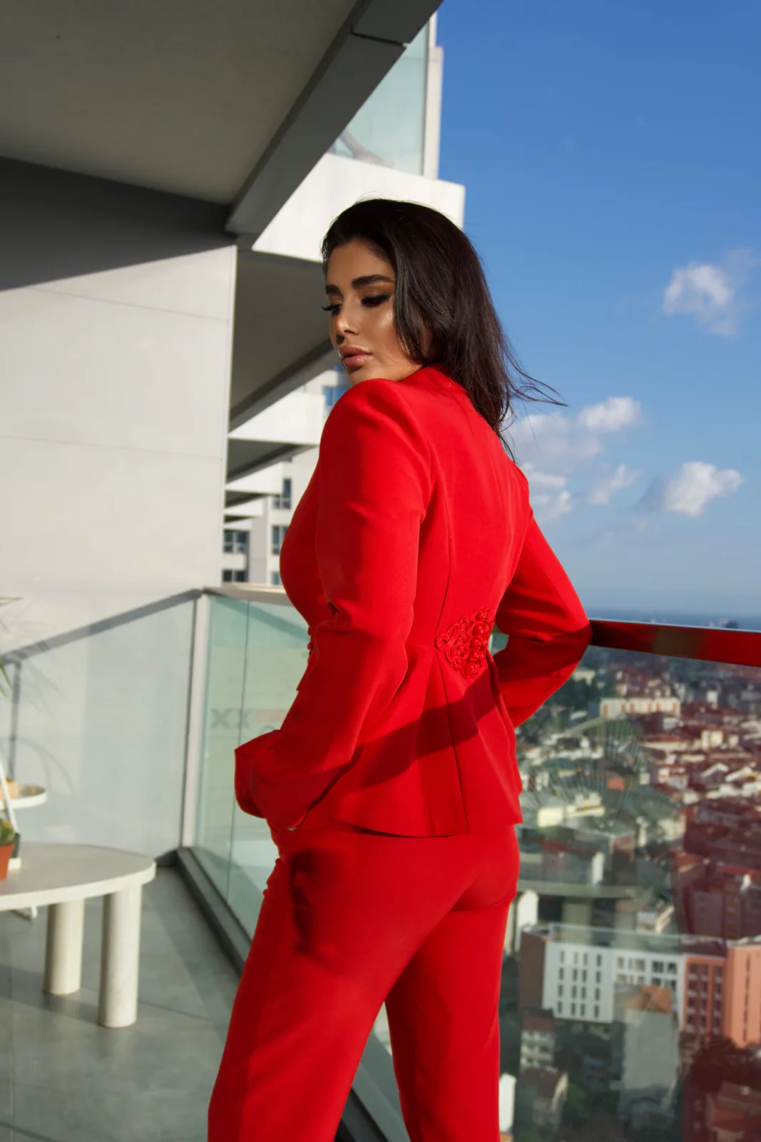 Red peplum suit, model looking out over the city from a glass balustrade