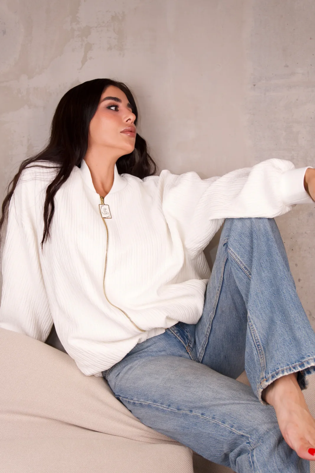 Ecru crinkle bomber, model seated with hair down on a cream sofa