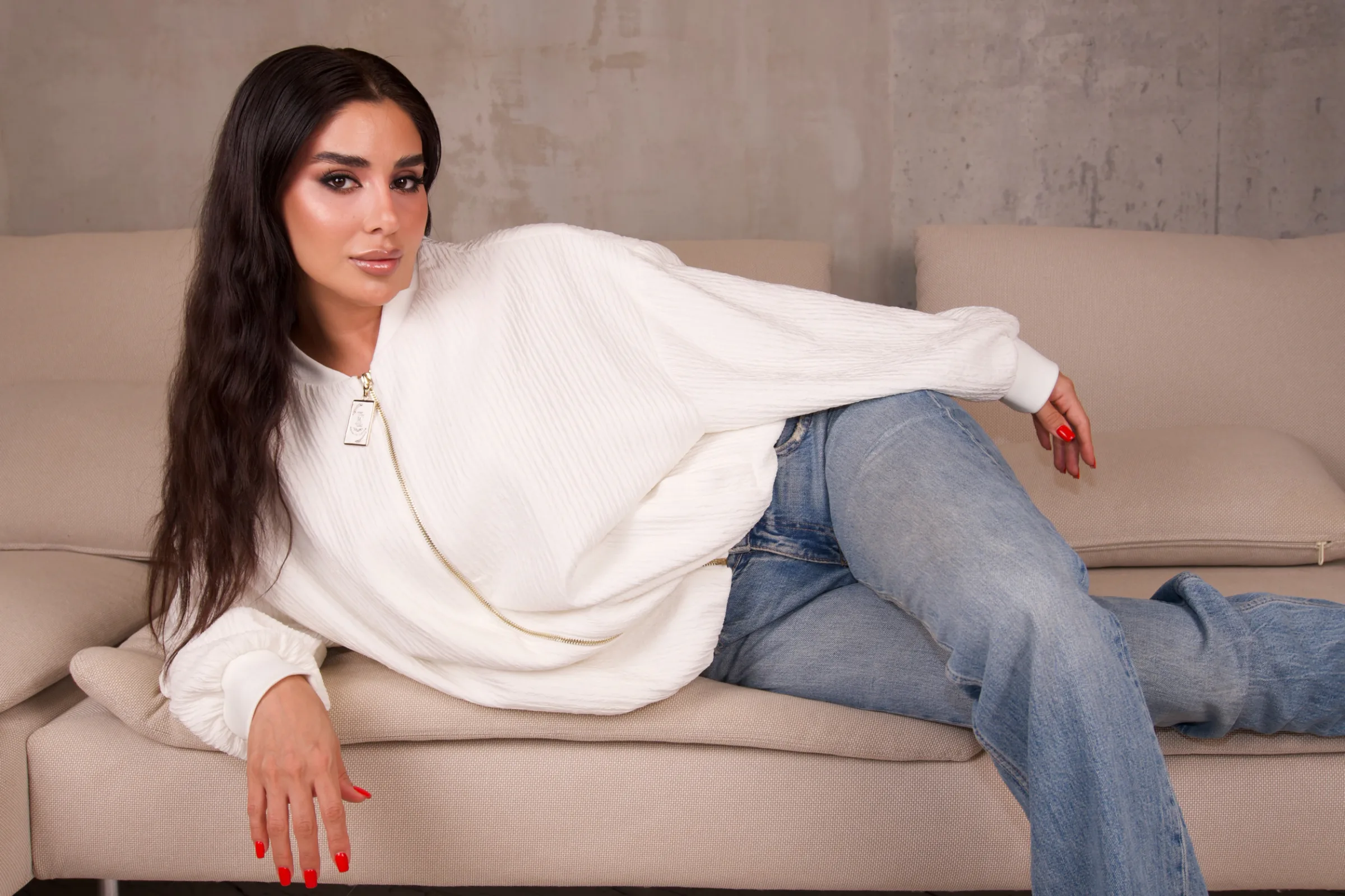 Ecru crinkle-texture bomber, model lying back on a cream sofa in light denim