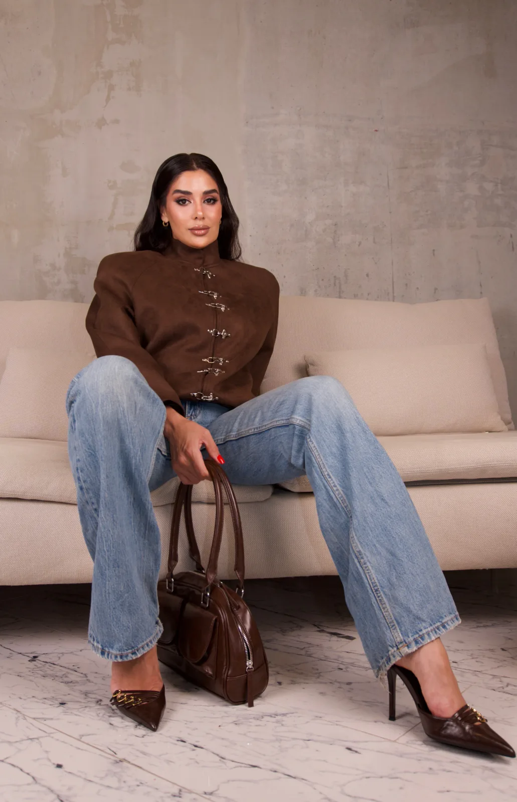 Brown suede bomber lying across a cream sofa with a brown leather bag on the floor