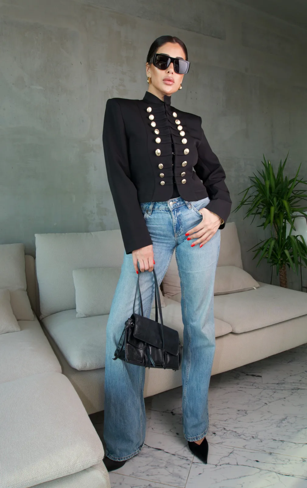 Black military jacket with gold buttons, standing with hands in denim pockets